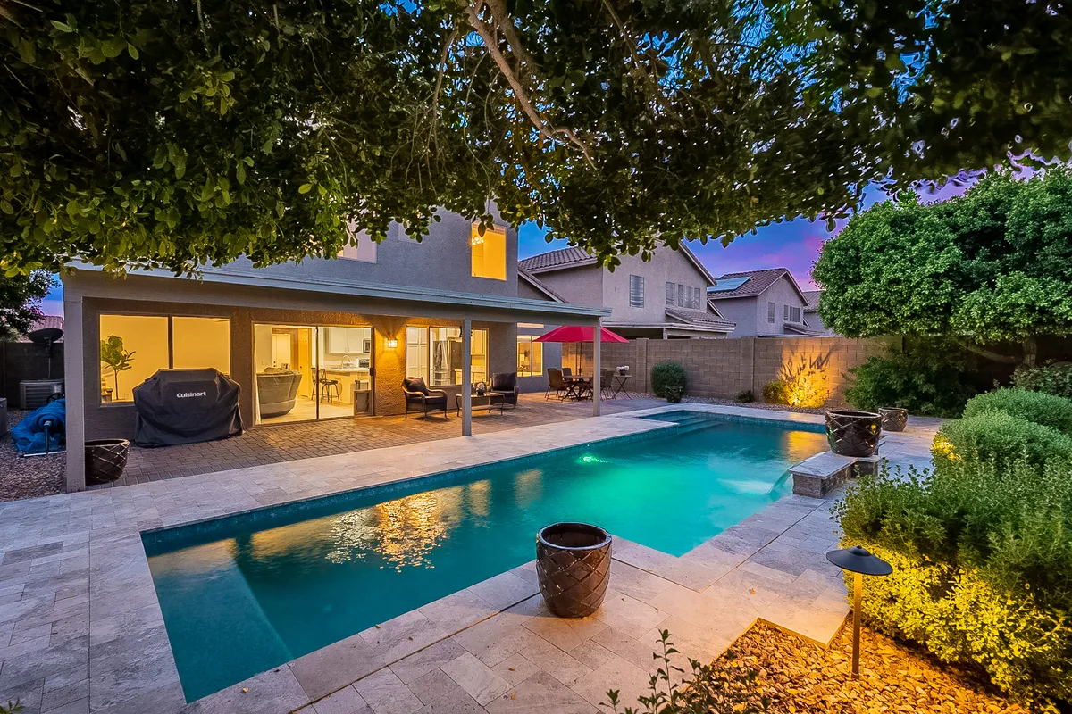 Twilight backyard pool framed by mature trees and a covered patio